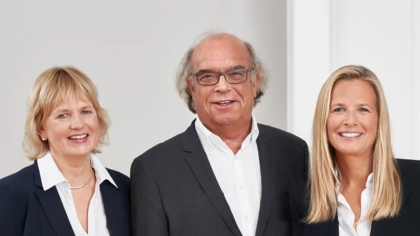 Drei Personen im Business-Outfit vor hellem Hintergrund, freundlich lächelnd