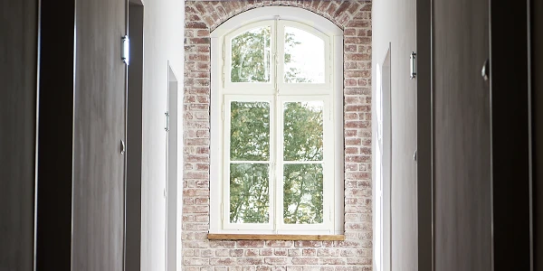 Flur mit Backsteinwand und großem Fenster, Blick ins Grüne