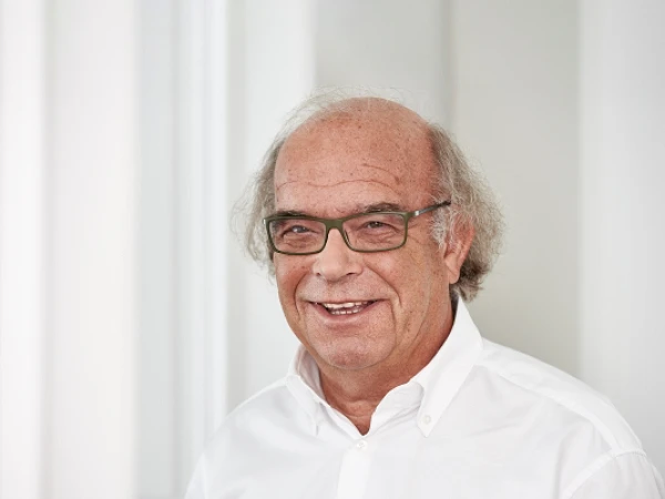 Älterer Mann mit Brille und weißem Hemd, freundlich lächelnd